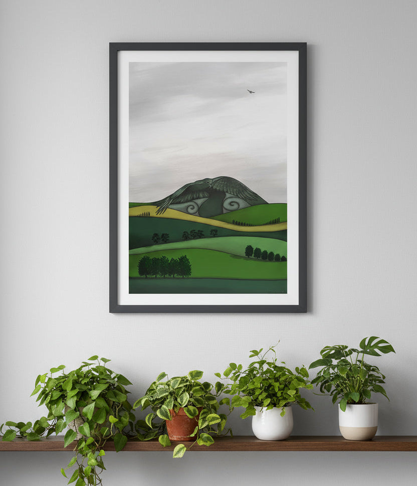 Framed artwork of a green landscape on a gray wall above a shelf with plants.