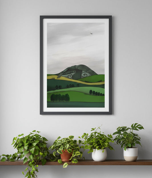 Framed artwork of a green landscape on a gray wall above a shelf with plants.